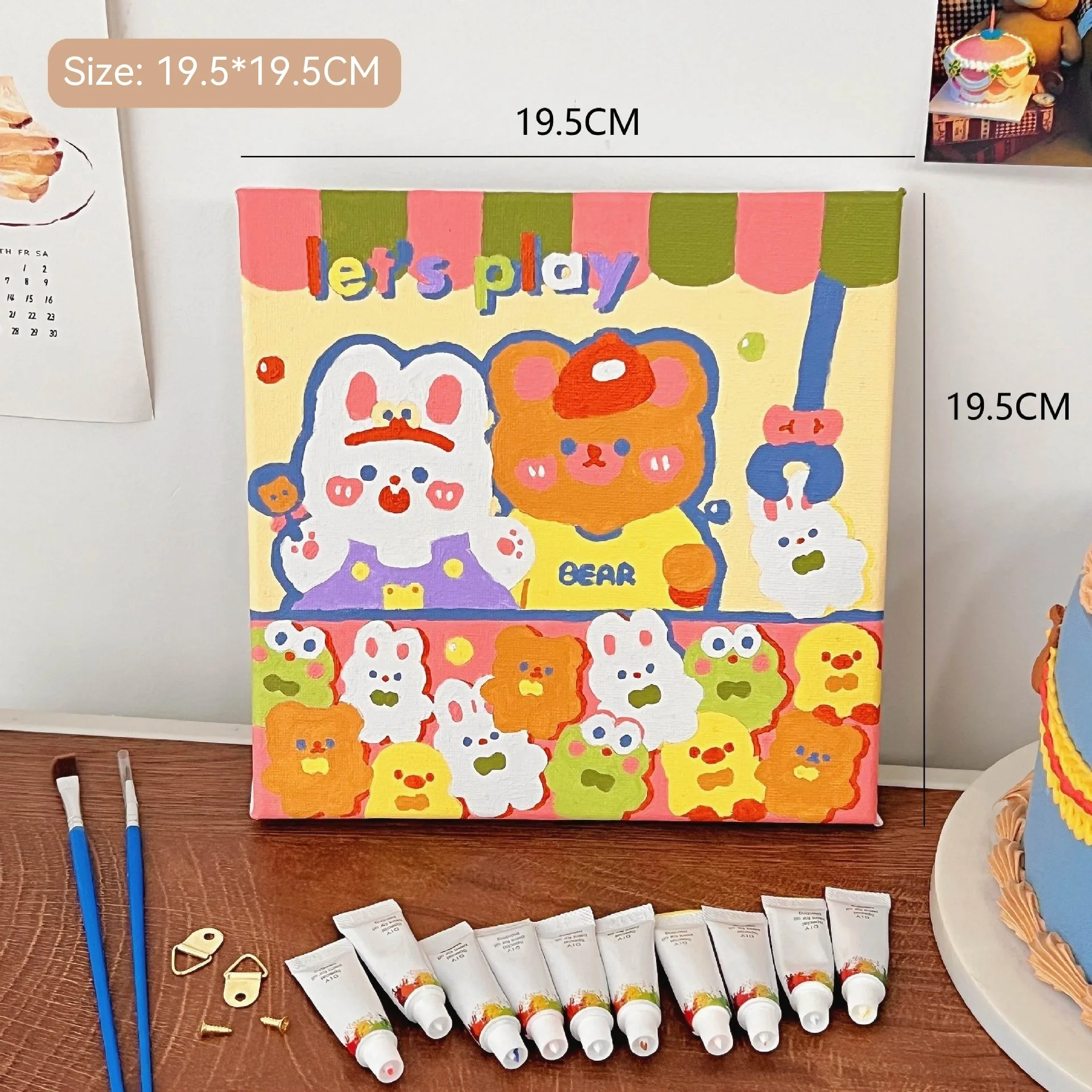 Mini DIY canvas painting kit with colourful “Let’s Play” bear design on a pre-printed canvas, including acrylic paint tubes and brushes arranged on a desk ready for painting