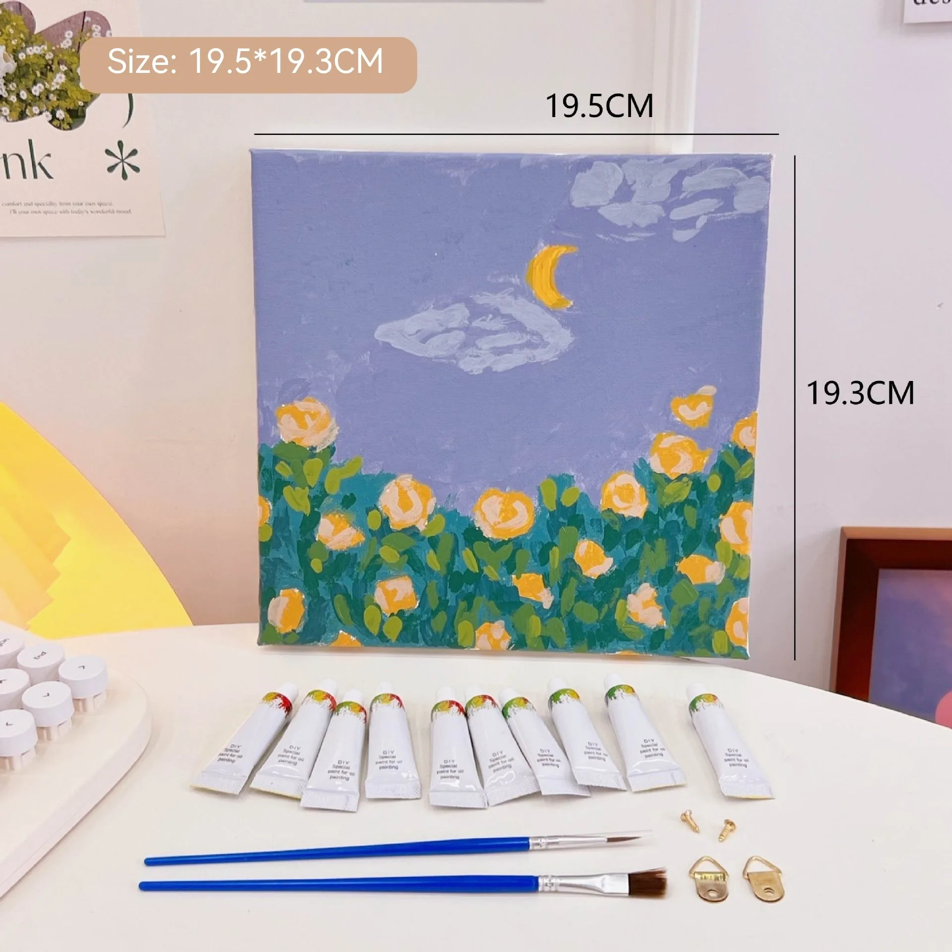 Mini DIY canvas painting kit with yellow rose garden under a crescent moon on a pre-printed canvas, including acrylic paint tubes and brushes arranged on a desk ready for painting