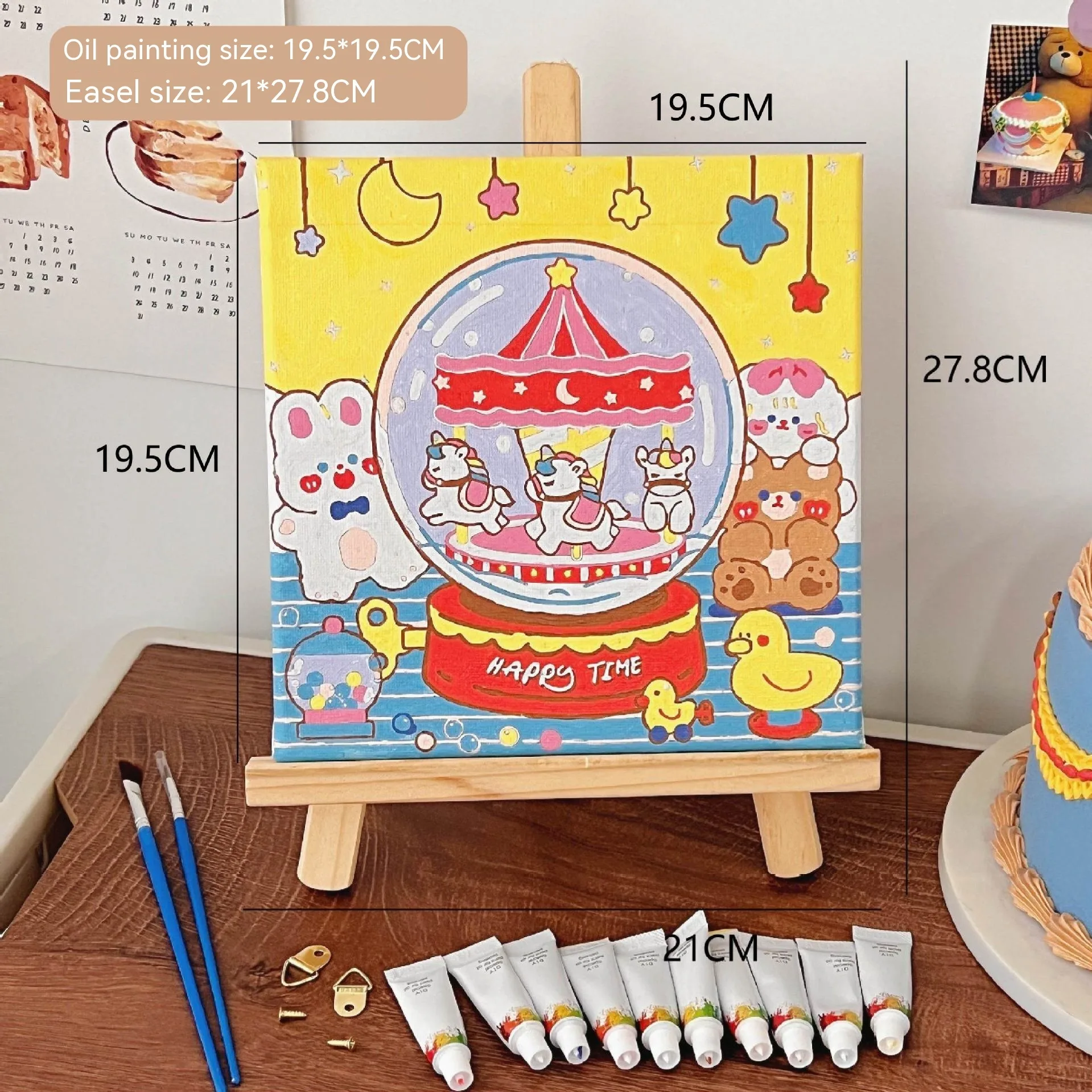 Mini DIY canvas painting kit featuring a carousel inside a crystal ball design on a small wooden easel, with acrylic paint tubes and brushes arranged on a desk ready for painting