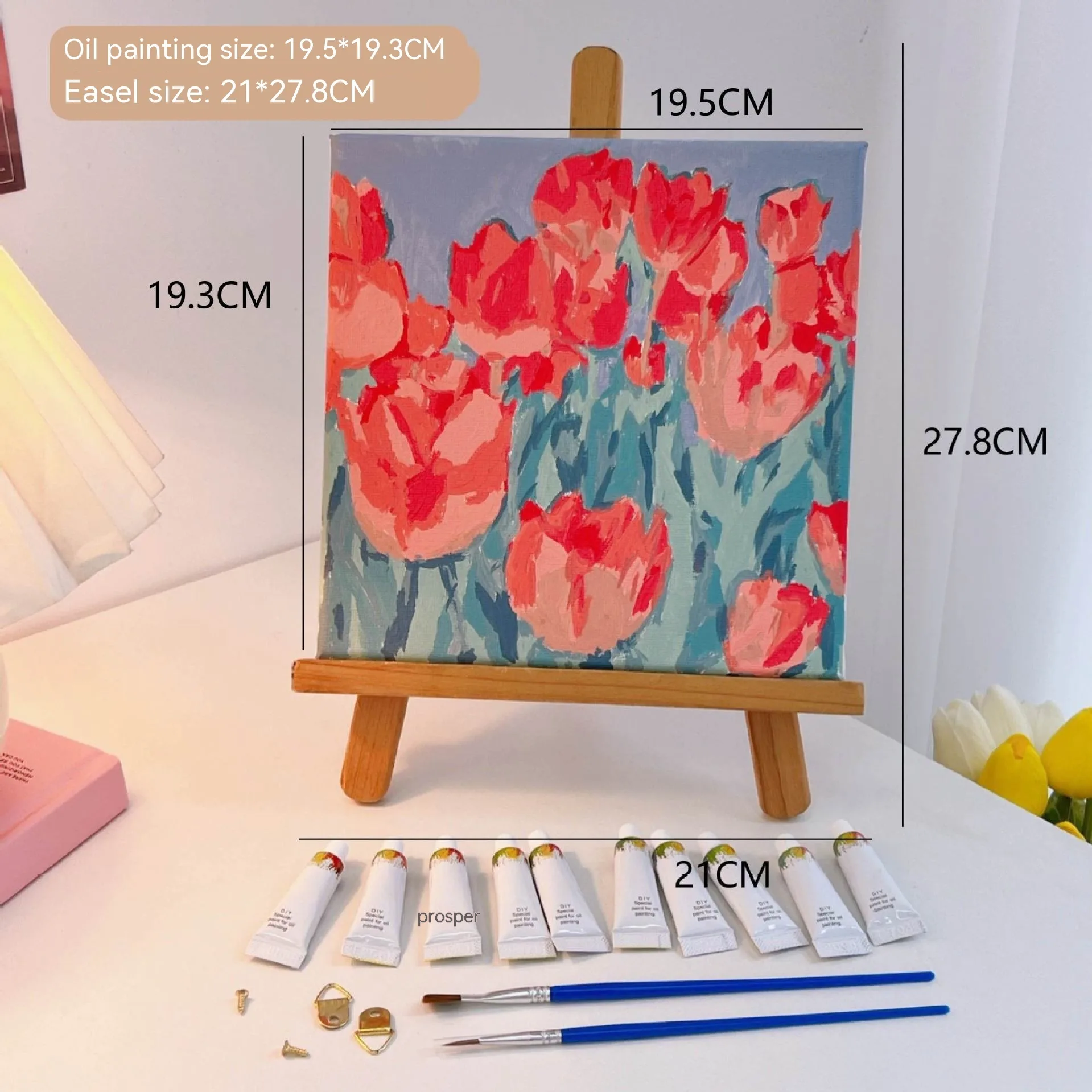 Mini DIY canvas painting kit featuring red flower field artwork on a small wooden easel, with acrylic paint tubes and brushes arranged on a desk ready for painting