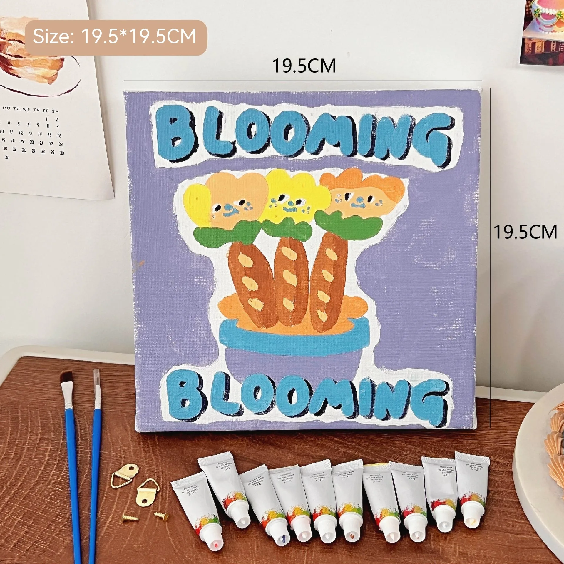 Mini DIY canvas painting kit with bread flowers blooming design on a pre-printed canvas, including acrylic paint tubes and brushes arranged on a wooden desk ready for painting