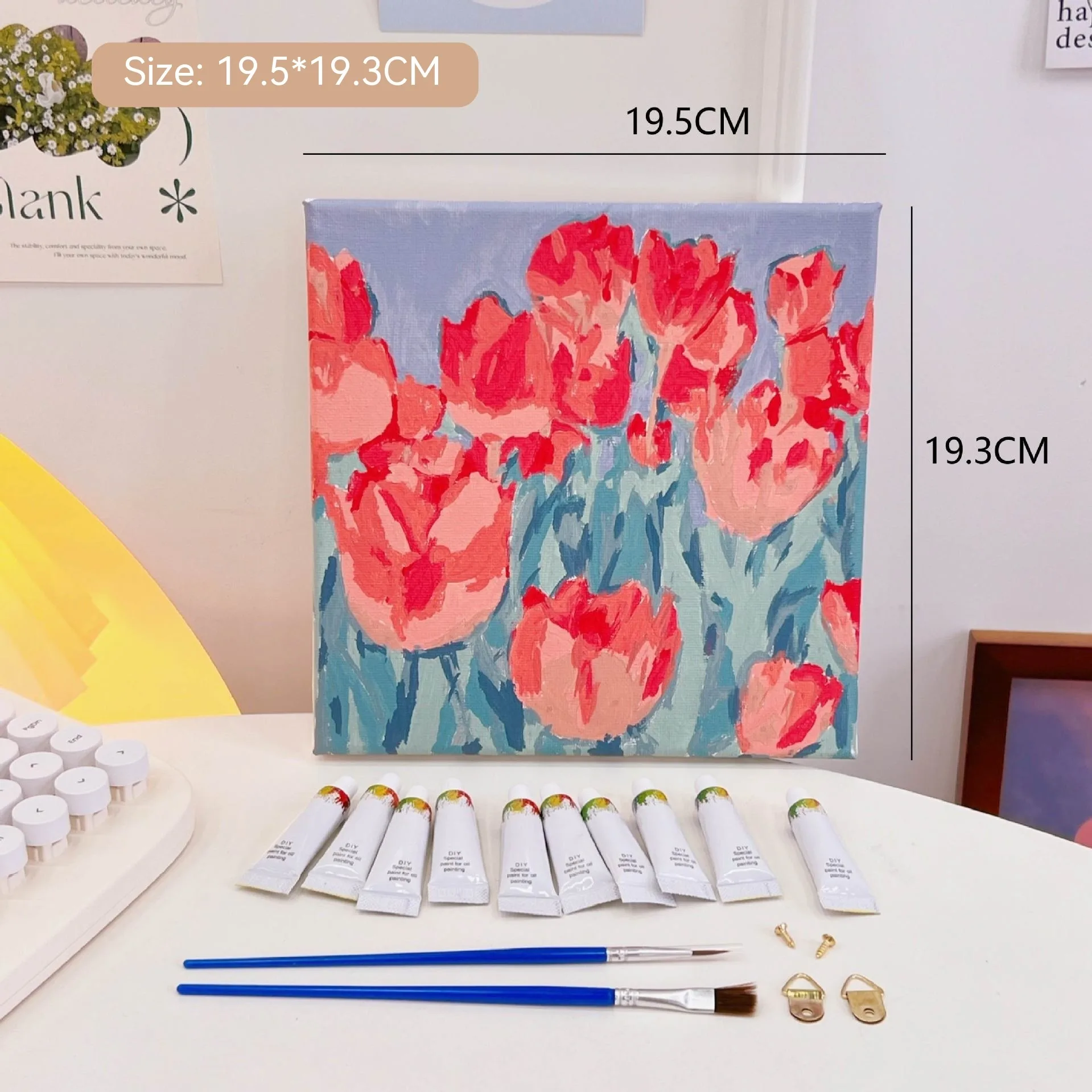 Mini DIY canvas painting kit with red flower field design on a pre-printed canvas, including acrylic paint tubes and brushes arranged on a desk ready for painting