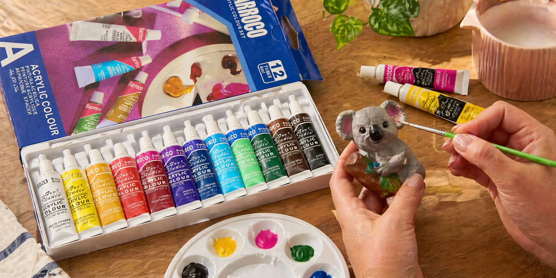 Acrylic paint set with brush in use, painting a small figurine on a wooden desk with palette and paint tubes in natural light
